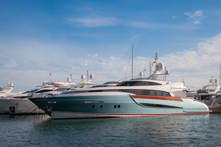 A blue and white yacht is docked along several other vessels under a clear sky.