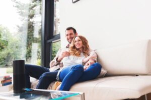 A couple on the couch with a Crestron remote and Amazon Alexa on the coffee table.